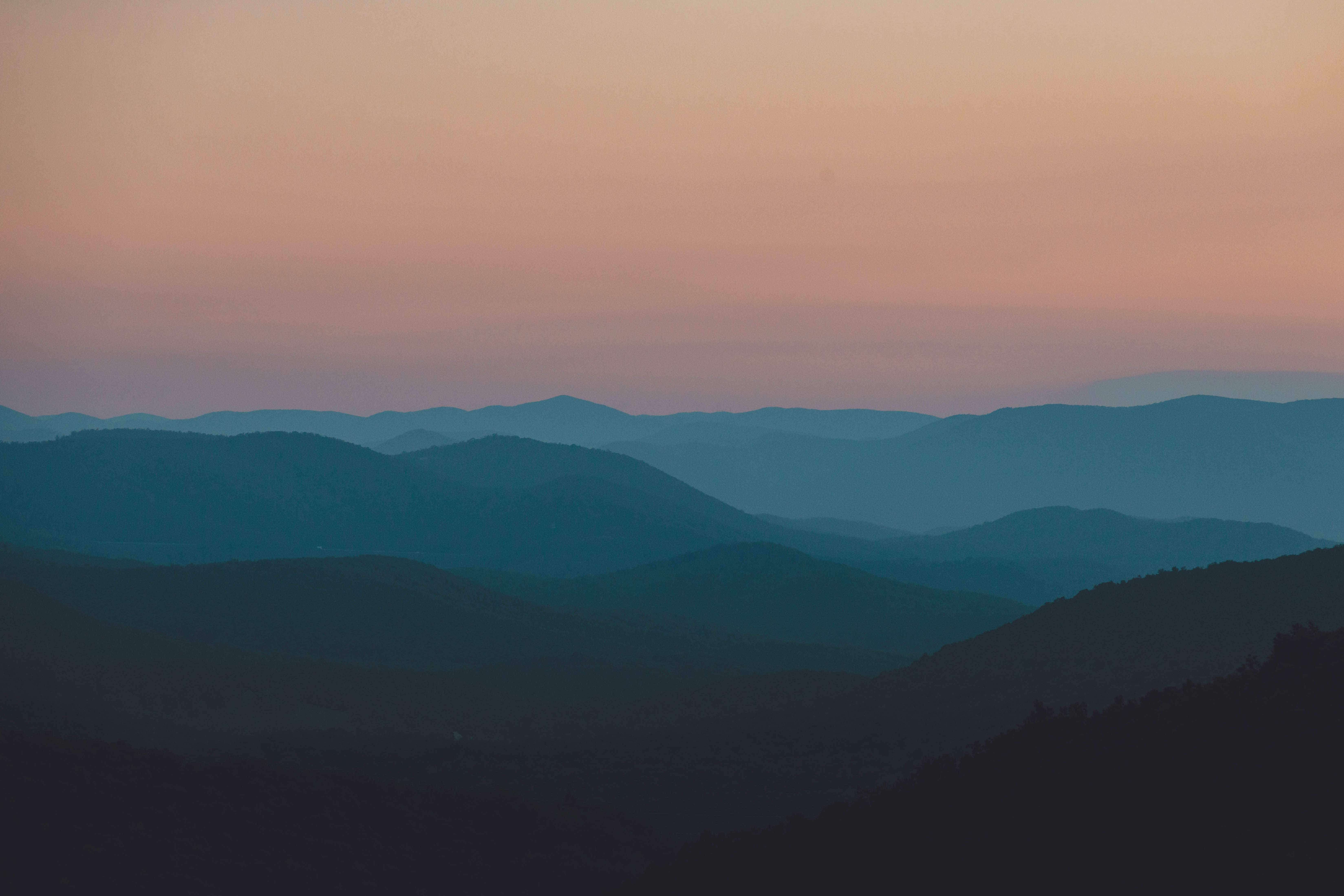 A beautiful bluish, reddish, hazy, aerial image of the Blue Ridge Mountains, taken during the golden hour in the Shenandoah National Park, Virginia. Published on Unsplash.com by Dave Herring